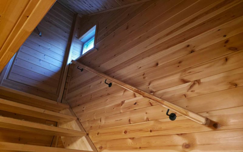 Wooden staircase in rustic house with pine wall cladding and railing. Interior design of cabin with natural light from small window. Construction and renovation concept for residential area.