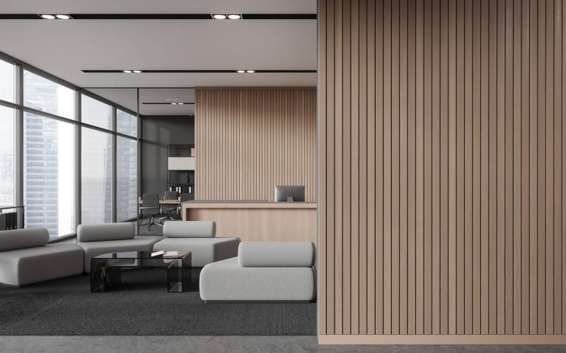 Interior of modern office hall with gray and wooden walls, concrete floor, cozy wooden reception counter with computers and white armchairs for visitors. Copy space wall. 3d rendering